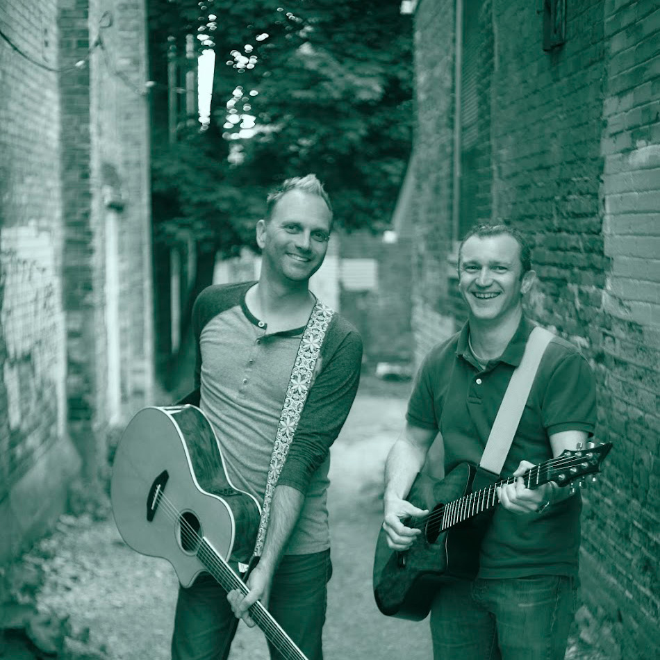two musical artists holding guitars and smiling at the camera